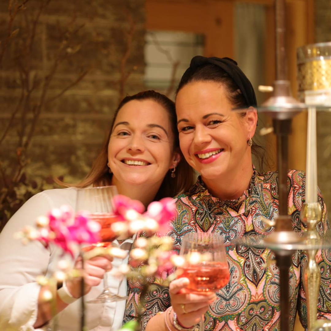 Zwei Frauen lächeln mit Weinglas der Hand.